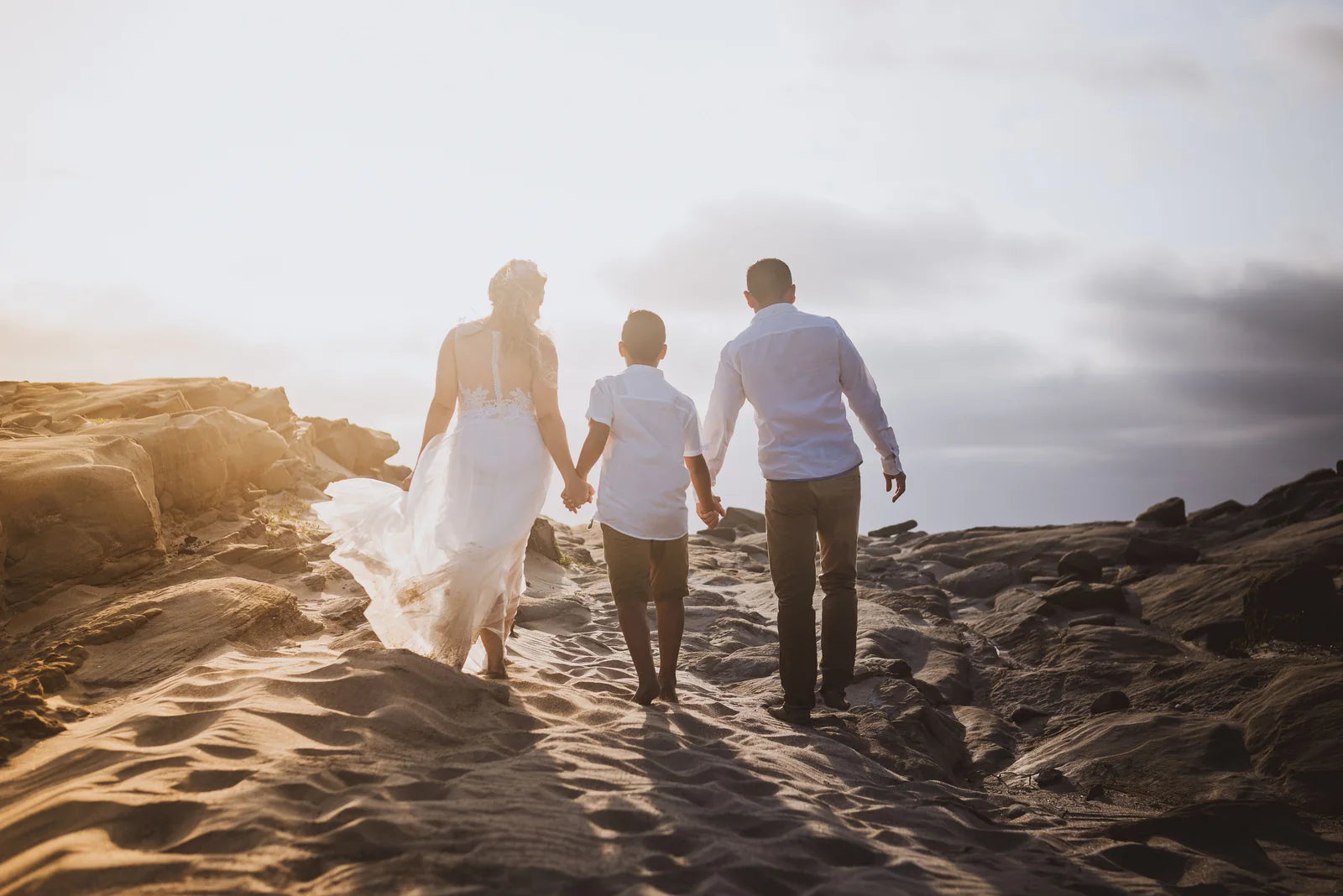 A family holding hands by the ocean in warm evening light.